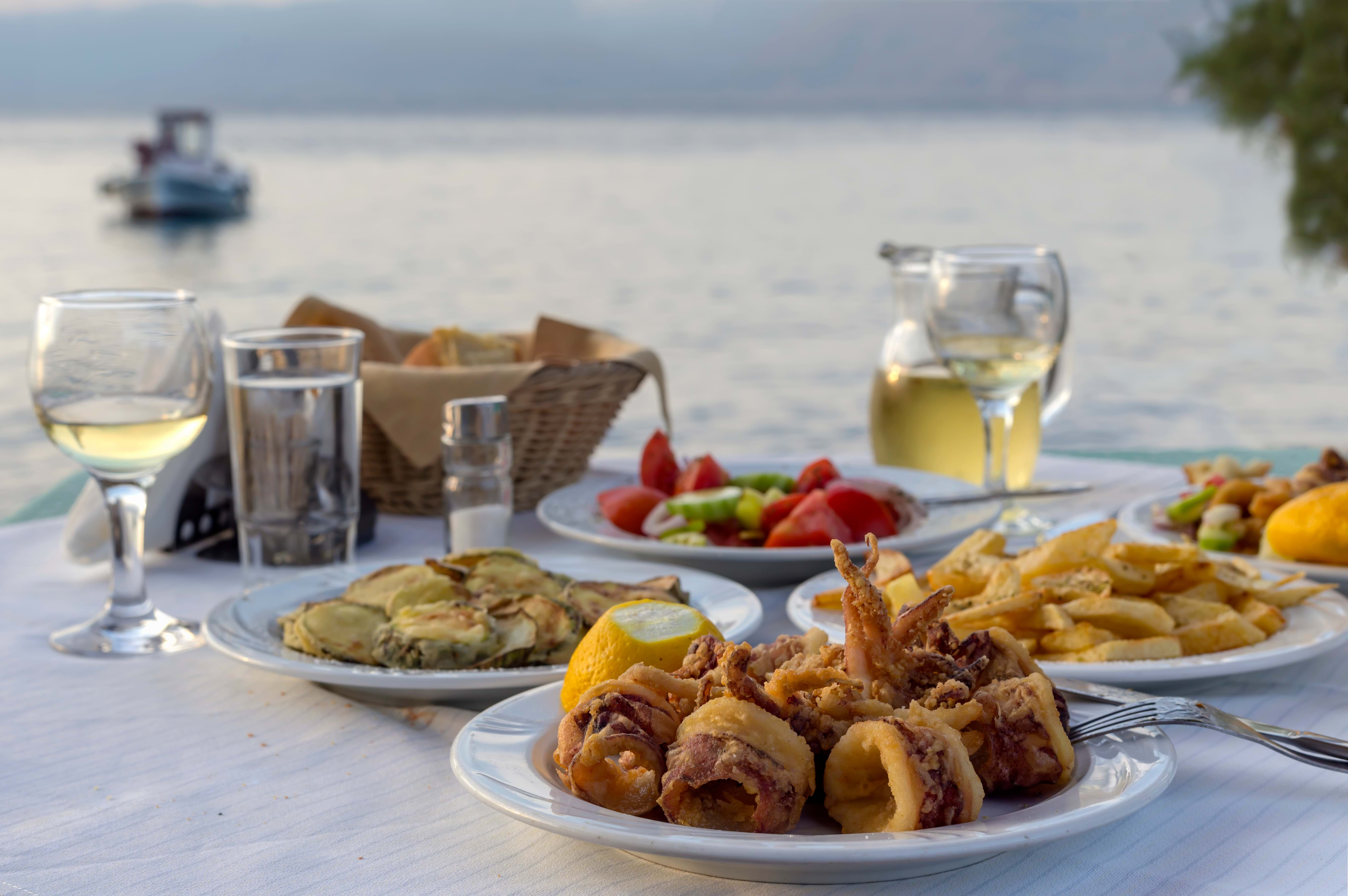 Traditional greek food, with fresh calamari, fries, cucumber, fried zucchini and tomato salad, served at a greek tavern by the sea. Image taken in the sunset.